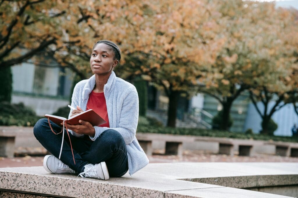black woman sitting on a bench outside with a journal in her hand, reflecting.